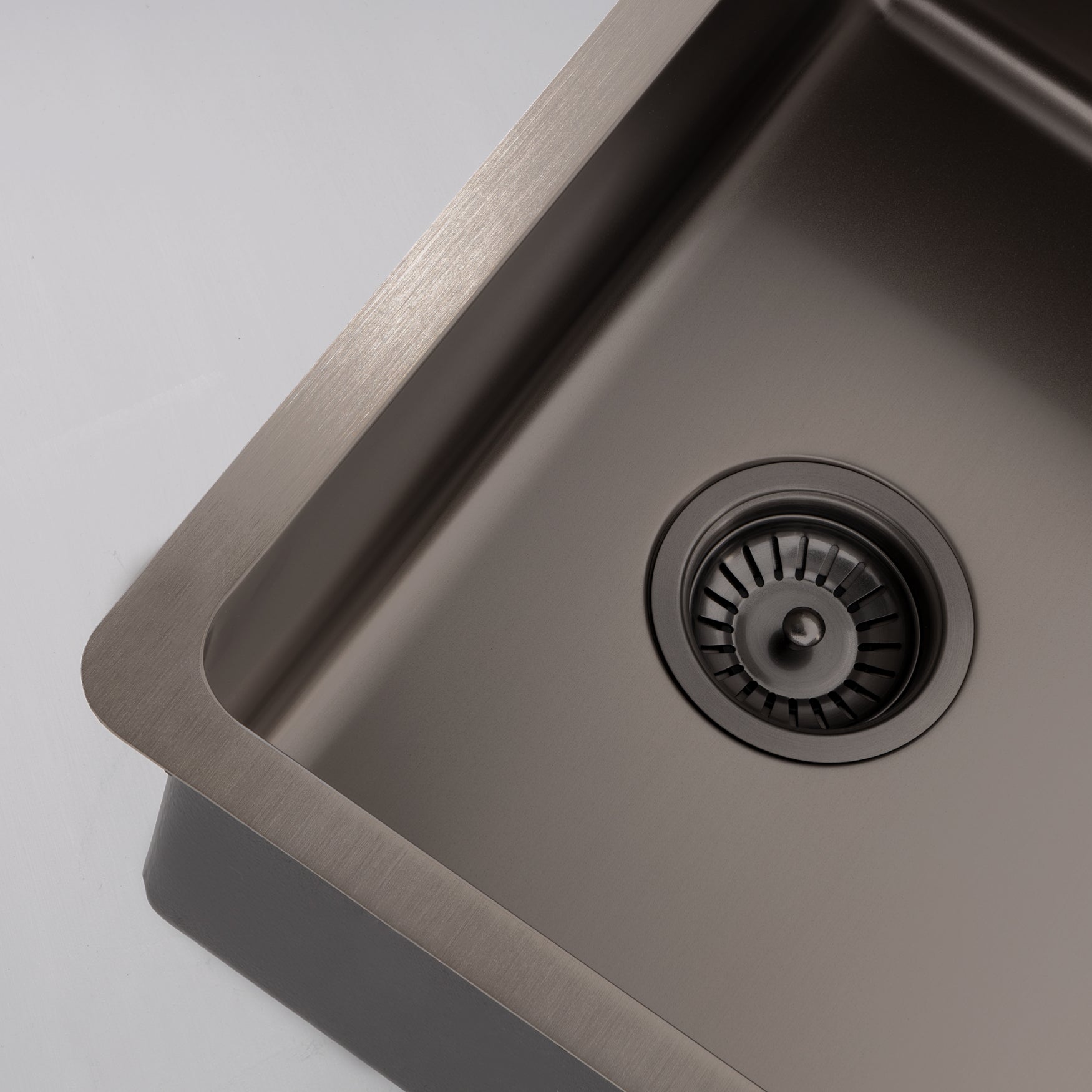 Close-up still life image of a Titan large bowl gunmetal sink for kitchen against a gray background, highlighting the elegant design of the brass sink.